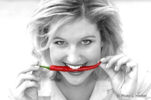 Schwarz/Weiß Portrait Foto mit roter Paprika zwischen den Zähnen
